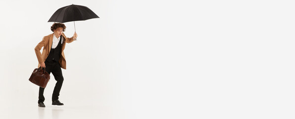 Portrait of young man, businessman dressed in suit in 50s, 60s fashion style going with umbrella isolated on white background. Retro vintage style, business, ad, emotions