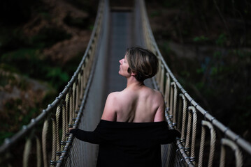 30 yo white woman standing on a simple suspension bridge outdoors at dusk