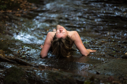 Naked 30 yo white woman resting on her arms in the water of the River Kyll, Kordel