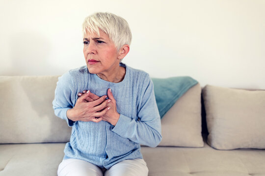 Shot of a beautiful matre woman holding her chest in discomfort due to pain at home during the day. A stressed woman who is suffering from a chest pain and touching her heart area.