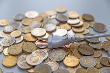 White electric plug, placed on a background of Euro coins. Increase in electricity bills, increases in electricity and energy costs.
