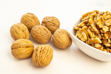 Walnuts in shell next to bowl containing shelled walnuts. Pruduction and consumption of nuts. Nutrition and properties of walnuts.
