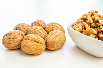 Walnuts in shell next to bowl containing shelled walnuts. Pruduction and consumption of nuts. Nutrition and properties of walnuts.
