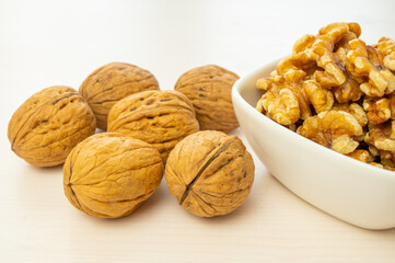 Walnuts in shell next to bowl containing shelled walnuts. Pruduction and consumption of nuts. Nutrition and properties of walnuts.
