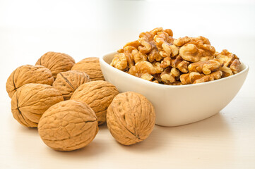 Walnuts in shell next to bowl containing shelled walnuts. Pruduction and consumption of nuts. Nutrition and properties of walnuts.
