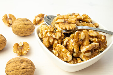 Walnuts in shell next to bowl containing shelled walnuts. Pruduction and consumption of nuts. Nutrition and properties of walnuts.
