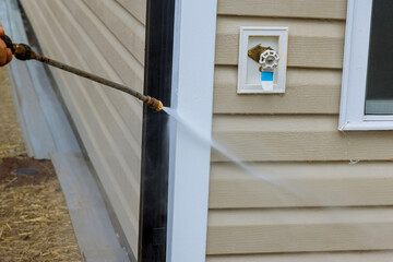 Maintenance service of washing siding houses uses high pressure nozzles to spray water soap cleaner at high pressure to clean