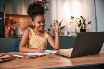 Having online study. Cute black girl in casual clothes is at home at daytime