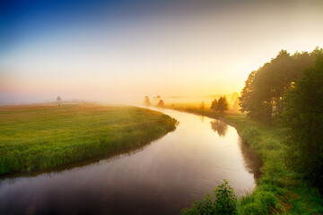 Obraz na płótnie Canvas Landscape sunset in Narew river valley, Poland Europe, foggy misty meadows with trees, spring time