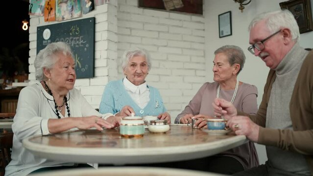 Happy senior friends sitting indoors in cafe drinking coffee or tea, laughing and having nice time together.