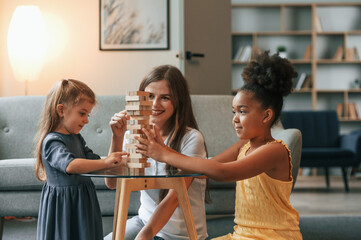 A young woman with two girls is playing a wooden tower game indoors together