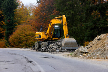 Detail view of a big excavator used to destroy old asphalt road on a mountain road in autumn season. Industrial machines used in transportation industry.