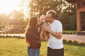 Kissing the baby. Happy parents with their son newborn outdoors having a weekend