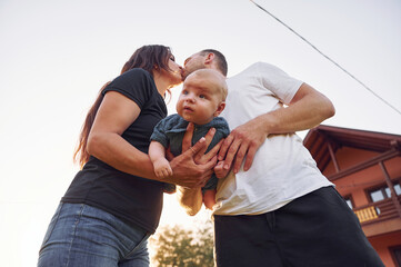 Kissing each other. Happy parents with their son newborn outdoors having a weekend