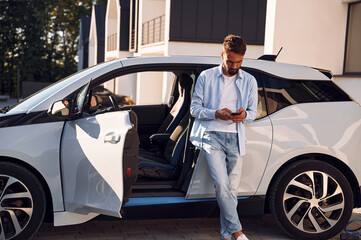 Young stylish man is with electric car at daytime
