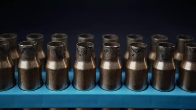 Slow motion pan upwards over empty bullet cases. Bullet shells in a blue container in three rows. 
