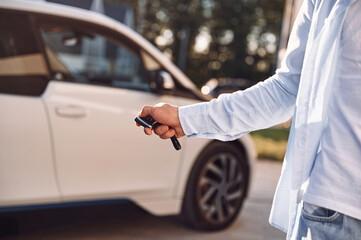 Standing with keys and locking the automobile. Close up view of man with his electric car