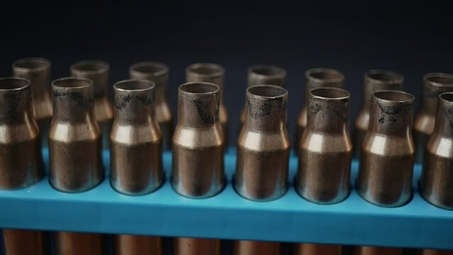 Slow motion horizontal pan across empty bullet cases. Bullet shells in a blue container in three rows. 