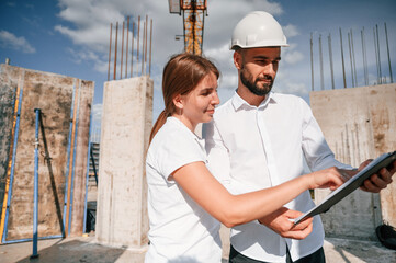 Reading the document in notepad. Man in uniform working with woman on the construction site