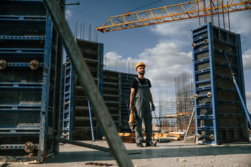 Standing with grinding machine in hands. Man in uniform is working on the construction site