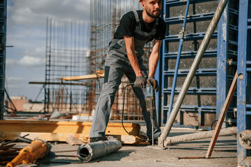 Using the drill. Man in uniform is working on the construction site