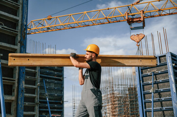 Against crane with wooden plank. Man in uniform is working on the construction site