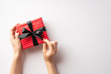 Black friday concept. First person top view photo of female hands untying ribbon bow on red giftbox on isolated white background with copyspace