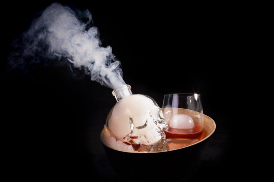 A bottle in the form of a skull with a cocktail and a stream of smoke, an alcoholic cocktail based on rum, a glass with a drink and ice