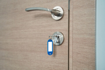 A key with a blank keychain in the lock of a wooden door close up. High quality photo