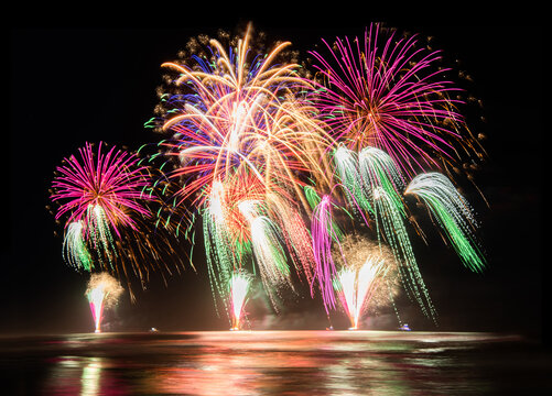 Multi coloured fireworks exploding over an ocean in the night sky.