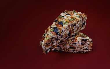 Two pieces of gozinak from various nuts with dried fruits on a red background.