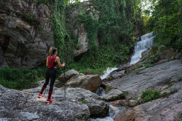 Obraz premium Young fitness woman running at forest trail on waterfall background