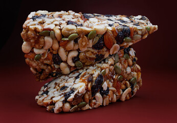 Two pieces of gozinak from various nuts with dried fruits on a red background.