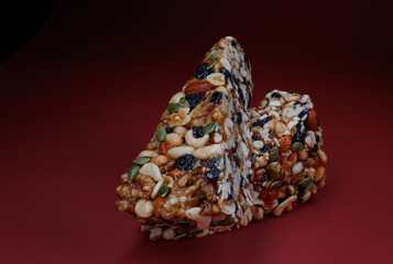 Two pieces of gozinak from various nuts with dried fruits on a red background.