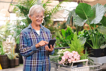 Senior caucasian woman in checkered shirt enjoying shopping in the greenhouse selecting pots of plants and flowers for her garden