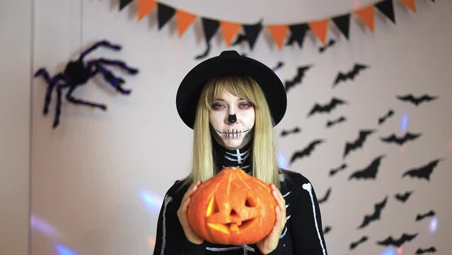 pretty young woman in skeleton costume holding pumpkin in hands at halloween party
