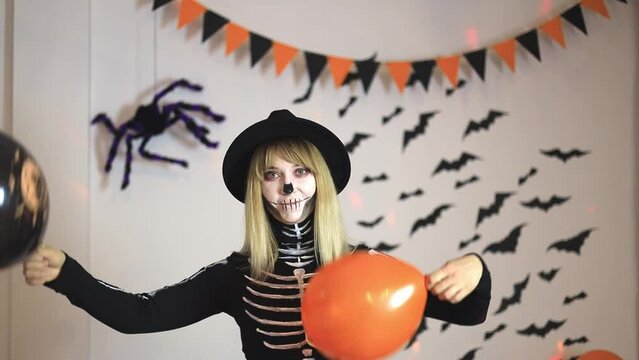 Pretty woman in skeleton costume dancing at halloween party with balloons