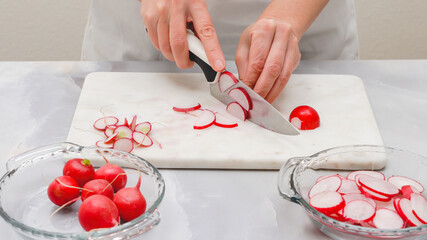 Fresh sliced radish close up on marble cutting board on light greybackground. Vegetable salad preparation process, recipe