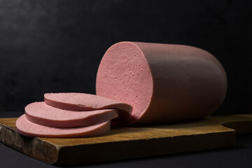 Boiled sausage on a wooden board on a black background. Sliced boiled sausage.