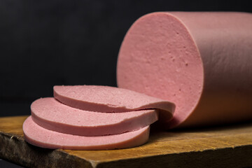 Boiled sausage on a wooden board on a black background. Sliced boiled sausage.