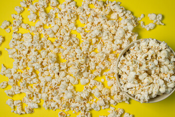 A plate full of popcorn on a yellow background. Delicious salty popcorn