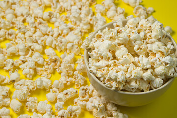 A plate full of popcorn on a yellow background. Delicious salty popcorn