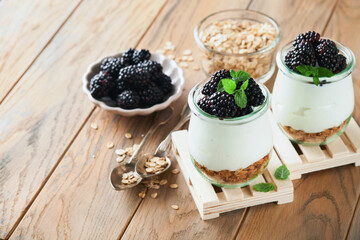 Yogurt with granola, blackberry berry fruits and muesli served in glass jar on wooden background....