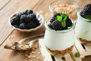 Yogurt with granola, blackberry berry fruits and muesli served in glass jar on wooden background. Healthy breakfast concept. Healthy food for breakfast, top view