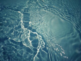 Bluewater waves on the surface ripples blurred. Defocus blurred transparent blue colored clear calm water surface texture with splash and bubbles. Water waves with shining pattern texture background.