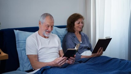 Happy senior couple reading books together in their bed. - Powered by Adobe