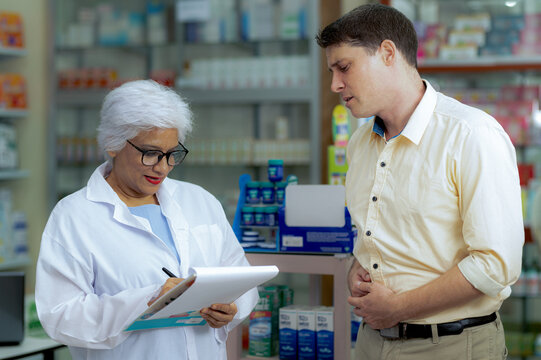 A young man consults a pharmacist to buy medicine for stomach pain.