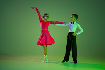 Studio shot of graceful little boy and girl dancing ballroom dance isolated over green background...