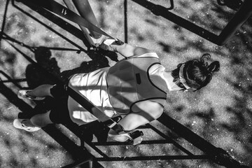 Concentrated, healthy and fit young latin man with weight vest, workout gloves and visor performing exercises with elastic bands on bars in a workout park in sunny day (in black and white)