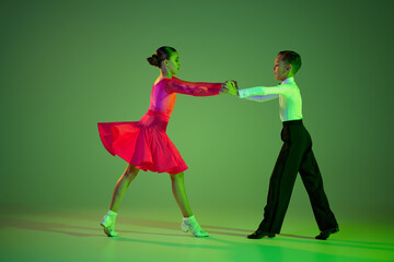 Studio shot of graceful little boy and girl dancing ballroom dance isolated over green background...